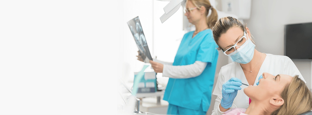 A dental professional wearing safety PPE gear and white lab coat smiling compassionately