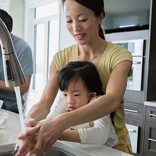 Mother and daughter washing hands while enjoying time with the whole family in the kitchen